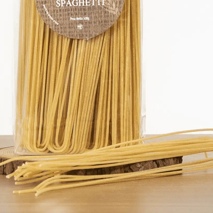 Pacchetto di spaghetti e alcuni spaghetti sparsi su un tavolo di legno.